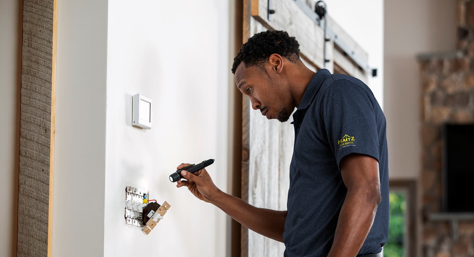 A professional Maitz electrician using a flashlight to safely inspect and troubleshoot exposed residential wall switch wiring during an electrical repair service.