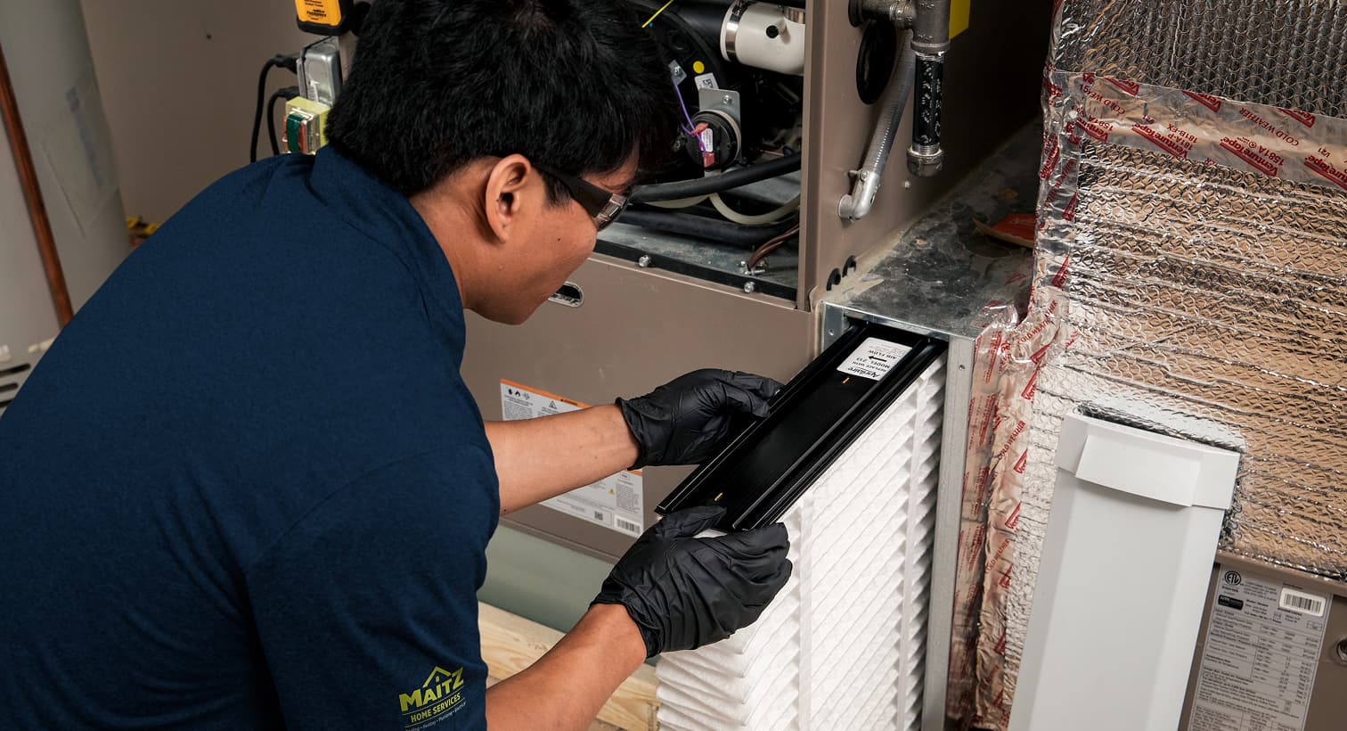 A professional Maitz HVAC technician replacing a clean pleated air filter in an indoor air handler unit during a routine AC maintenance tune-up.